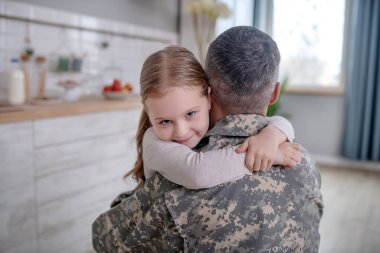 Little girl hugging a mans neck in a uniform.