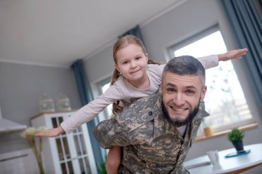 Dad officer and little daughter play airplane at home.
