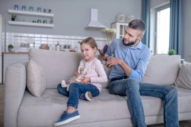 Young caring dad combing hair to little daughter.