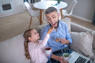 Little caring daughter giving dad a tasty cookie.