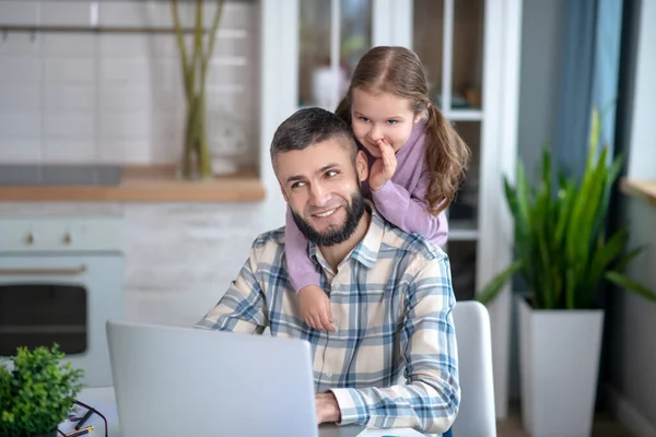 Vader zit met laptop, dochter fluistert van achteren in het oor. — Stockfoto