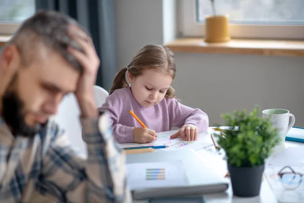 テーブルの上に小さな女の子の絵と疲れたお父さん. — ストック写真