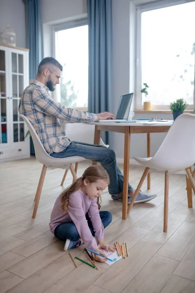 Dad working at the table, daughter sitting on the floor.