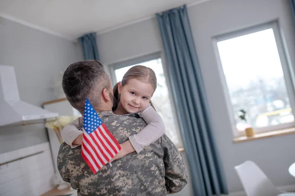 Kleines Mädchen mit der amerikanischen Flagge auf den Händen eines Offiziers. — Stockfoto