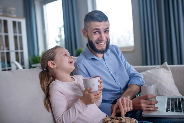 Тато і дочка з чаєм і печивом сидять на дивані . — стокове фото