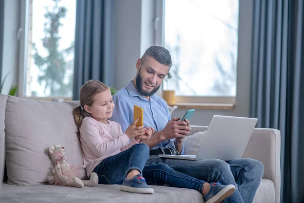 Dochter toont smartphone scherm aan papa, met smartphone en laptop. — Stockfoto