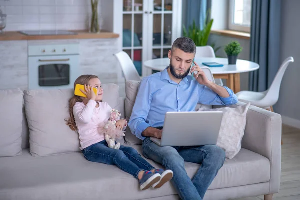 Papá con laptop y smartphone, hija pequeña con smartphone y juguete . — Foto de Stock