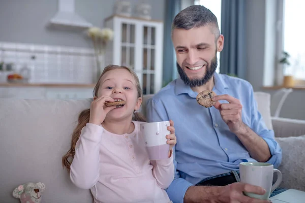 Маленька дочка з татом на дивані їсть печиво . — стокове фото