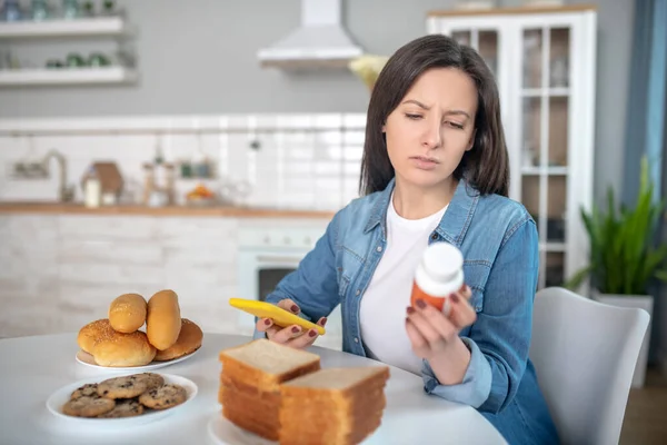 Mujer mirando las pastillas mientras está sentada en la cocina — Foto de Stock