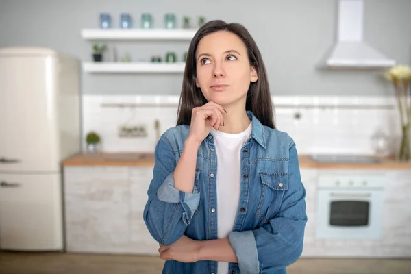 Bedachtzame jonge vrouw staat in haar keuken — Stockfoto