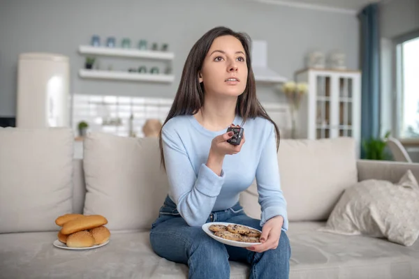 Nő eszik sütit és zsemlét közel a TV-hez — Stock Fotó