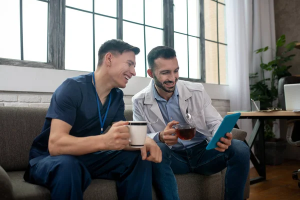 Dos médicos jóvenes tomando té y leyendo algo en una tableta — Foto de Stock