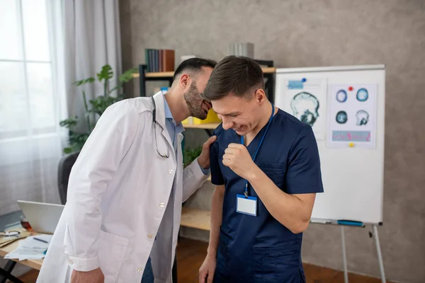 Médico barbudo diciendo algo gracioso en la oreja a su colega — Foto de Stock