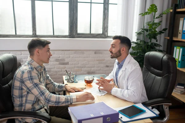 Paciente con camisa a cuadros explicando sus problemas al médico — Foto de Stock