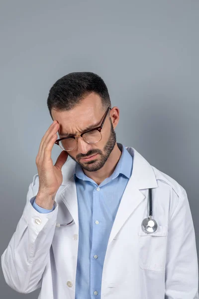Doctor in eyeglasses suffering from a headahce — Stockfoto