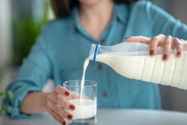 A woman pouring milk from the bottle to the glass