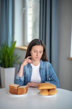 Thoughtful woman choosing between bread and pastry