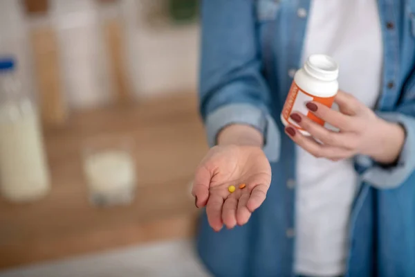 Femme tenant deux pilules et un récipient dans les mains — Photo