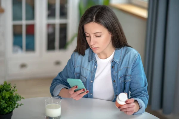 Mujer sosteniendo un teléfono inteligente y pastillas contenedor — Foto de Stock