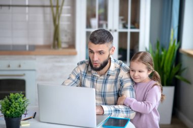 Young dark-haired dad and girl child looking at a laptop.