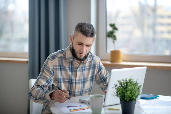 Young bearded man sitting and working with a chart. — Stockfoto
