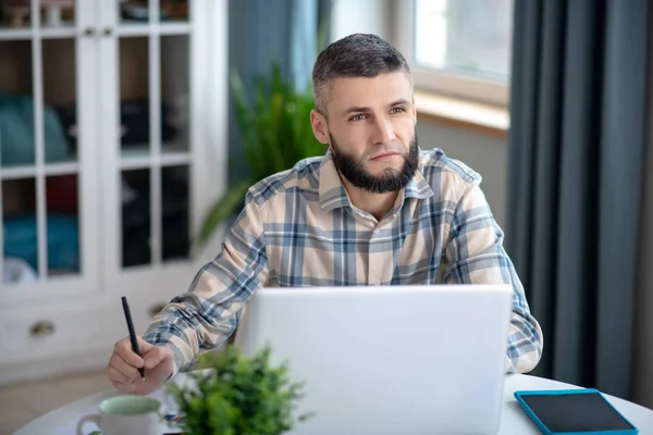 Jovem homem de cabelos escuros trabalhando atrás de um laptop branco . — Fotografia de Stock