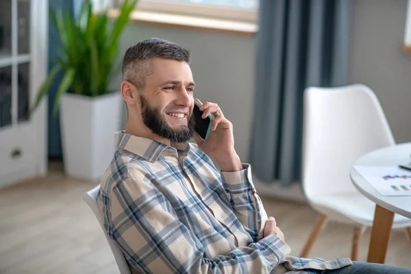 Young dark-haired man sitting and talking on a smartphone. — Stockfoto