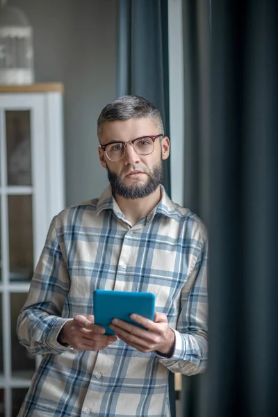 Young man in glasses with a tablet standing indoors. — ストック写真