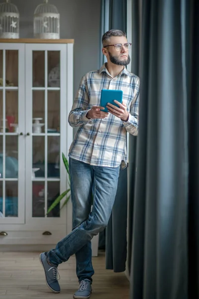 Young man in glasses with tablet standing by the window. — Stockfoto