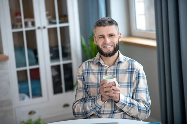 Happy young man sitting with a cup in his hands. — Stockfoto