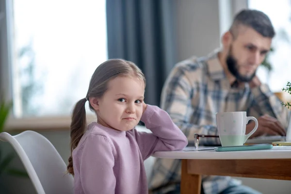 Menina sentada na mesa tristemente sorrindo, pai ocupado . — Fotografia de Stock