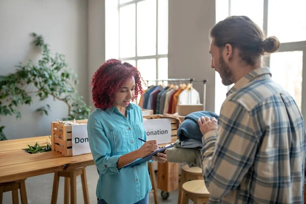 Chica joven haciendo notas, hombre con la ropa doblada en las manos . — Foto de Stock