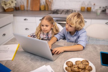 İki çocuk masada oturup internetten video izliyorlar.