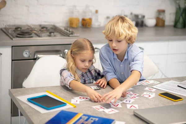 Two blond kids playing with letter cards and looking interested — Stock Photo, Image