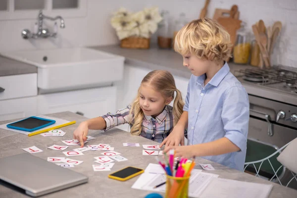 Zwei blonde Kinder legen Karten mit Buchstaben auf den Tisch — Stockfoto