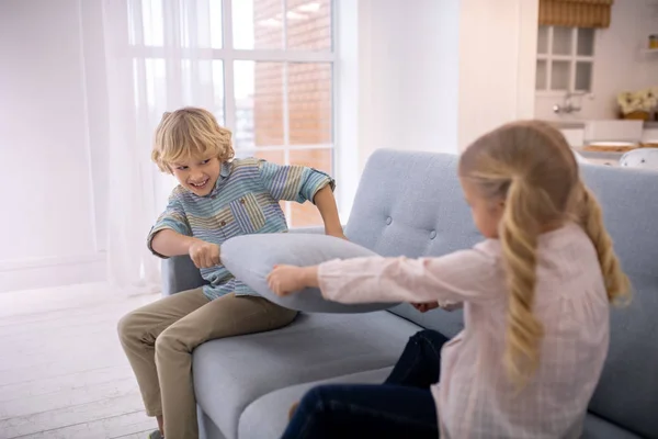 Due bambini biondi che giocano con i cuscini sul divano — Foto Stock