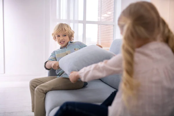 Due bambini biondi che giocano con i cuscini sul divano e sembrano cattivi — Foto Stock