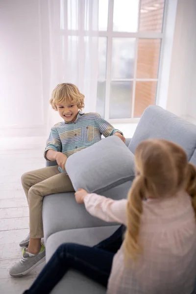 Dvě blonďaté děti si hrají s polštáři na gauči doma — Stock fotografie