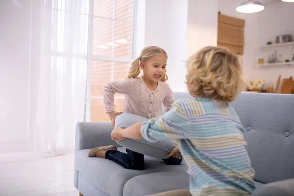 Twee blonde kinderen spelen met grijze sofa kussens — Stockfoto