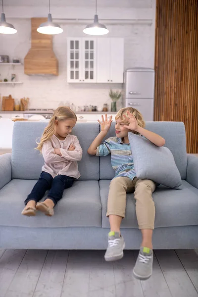 Rubio lindo chico con una almohada mostrando la lengua a su hermana — Foto de Stock