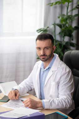 Beyaz cüppeli genç sakallı doktor gününü işte geçiriyor.