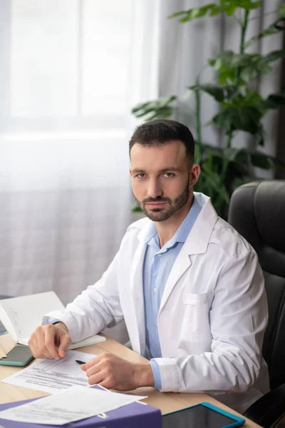 Mladý vousatý doktor v bílém rouchu tráví svůj den v práci — Stock fotografie