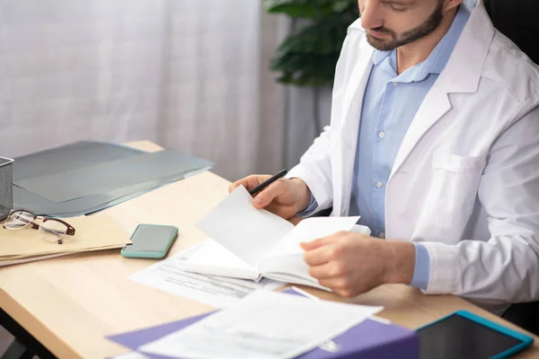 Jeune médecin barbu en robe blanche prenant des notes — Photo