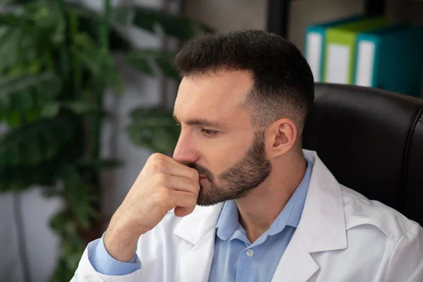 Dai capelli scuri medico barbuto in una veste bianca cercando stressato — Foto Stock