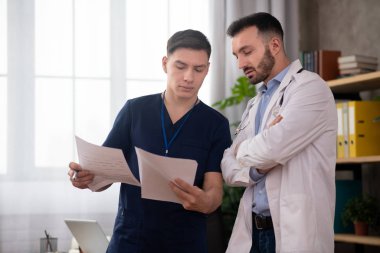 Değiş tokuş sırasında iki genç erkek doktor personel odasında tıbbi durumu tartışıyor.