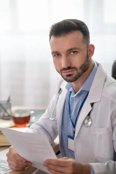 Giovane medico barbuto in una veste bianca avendo il suo tè del mattino — Foto Stock