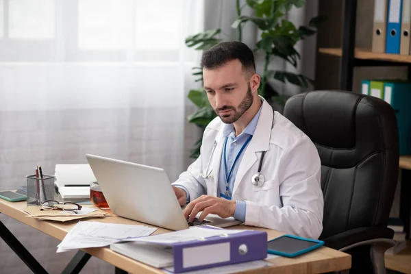 Giovane medico barbuto cercando coinvolti lavorando sul computer portatile — Foto Stock