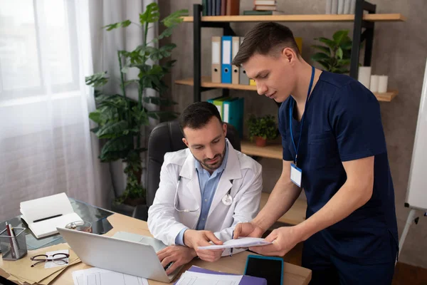 Jovem estagiário do sexo masculino discutindo caso médico com o médico chefe — Fotografia de Stock