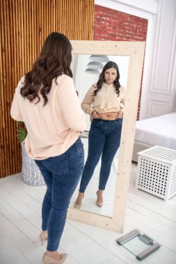 Young woman in a beige blouse looking at herself