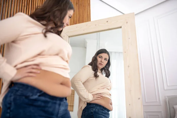 Jovem mulher em uma blusa bege de pé e olhando para seus abdominais — Fotografia de Stock